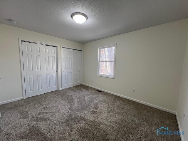 unfurnished bedroom featuring a textured ceiling, carpet, and two closets