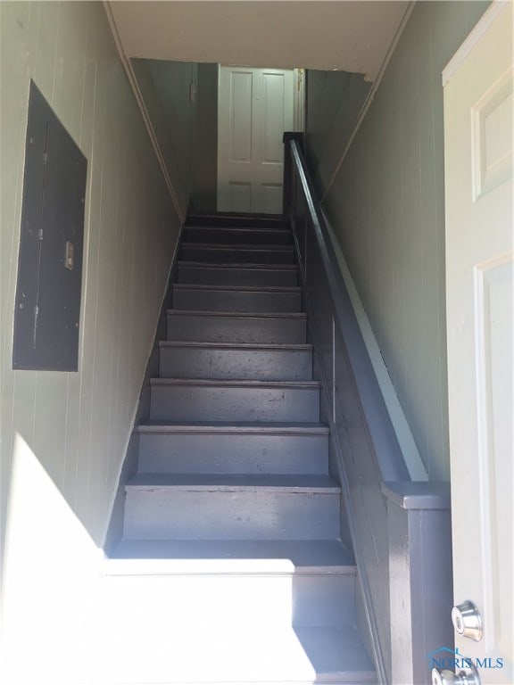 staircase featuring wood walls and electric panel