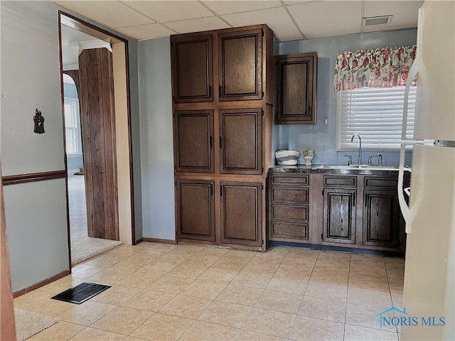 kitchen with a paneled ceiling, dark brown cabinetry, white fridge, and light tile patterned floors