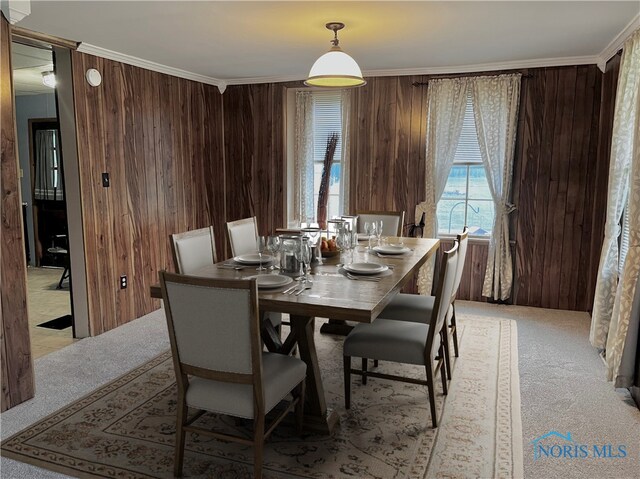 dining space with ornamental molding, light colored carpet, and wooden walls