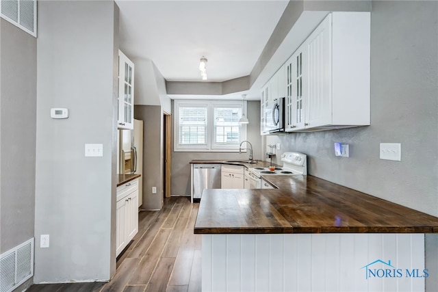 kitchen with wood-type flooring, white cabinetry, butcher block counters, kitchen peninsula, and appliances with stainless steel finishes