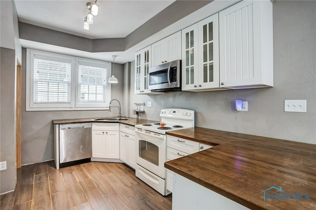 kitchen featuring appliances with stainless steel finishes, hanging light fixtures, white cabinets, wooden counters, and sink