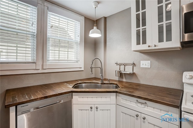 kitchen featuring white cabinets, pendant lighting, stainless steel appliances, sink, and wood counters