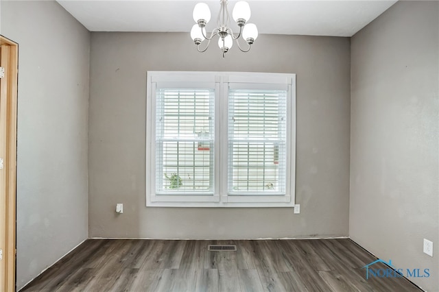 spare room featuring dark wood-type flooring and a chandelier