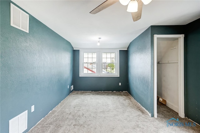 unfurnished bedroom featuring carpet floors, a closet, lofted ceiling, ceiling fan, and a walk in closet