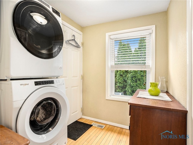 laundry area featuring light hardwood / wood-style flooring, stacked washer / drying machine, and cabinets