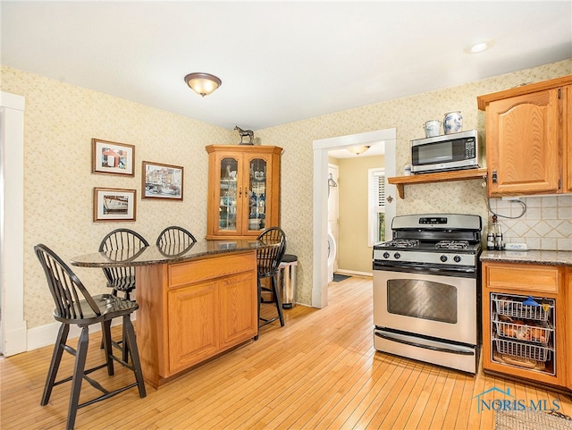 kitchen with dark stone countertops, a breakfast bar area, appliances with stainless steel finishes, and light hardwood / wood-style floors