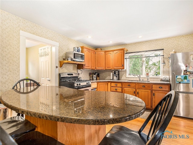 kitchen featuring light wood-type flooring, tasteful backsplash, sink, stainless steel appliances, and dark stone countertops