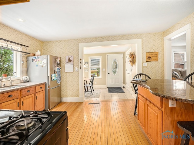 kitchen featuring light wood-type flooring, sink, black range, stainless steel refrigerator, and dark stone countertops