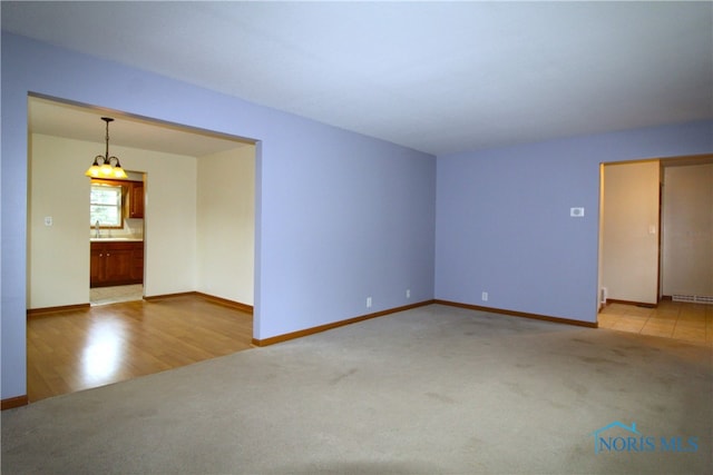 spare room with light carpet, sink, and a notable chandelier