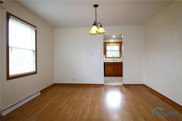 empty room featuring baseboard heating, an inviting chandelier, sink, and light wood-type flooring