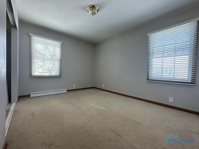 carpeted spare room featuring baseboard heating, plenty of natural light, and a textured ceiling