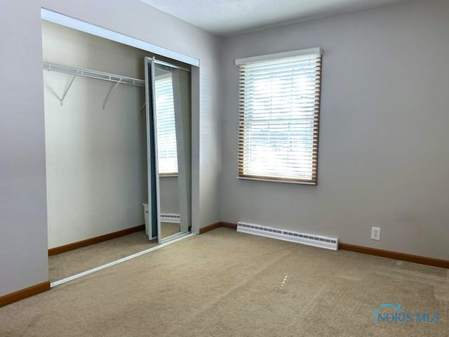 unfurnished bedroom with carpet floors, a baseboard heating unit, and a closet