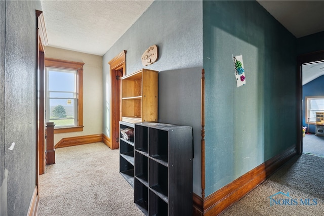 corridor with light carpet and a textured ceiling