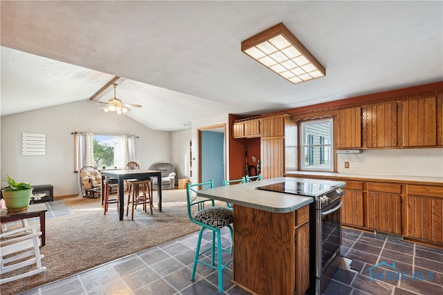 kitchen with electric range, a kitchen island, ceiling fan, vaulted ceiling, and dark colored carpet