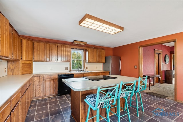 kitchen featuring a kitchen breakfast bar, black appliances, sink, and a kitchen island