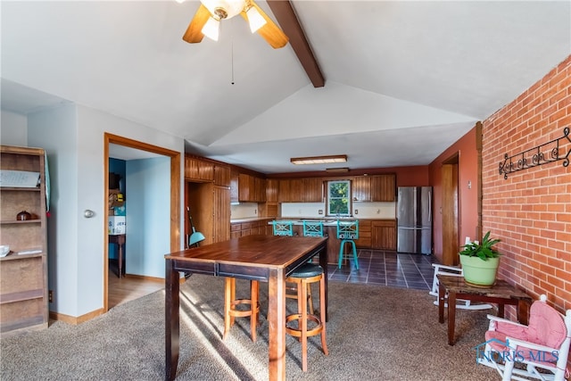 kitchen featuring lofted ceiling with beams, dark colored carpet, brick wall, and stainless steel fridge