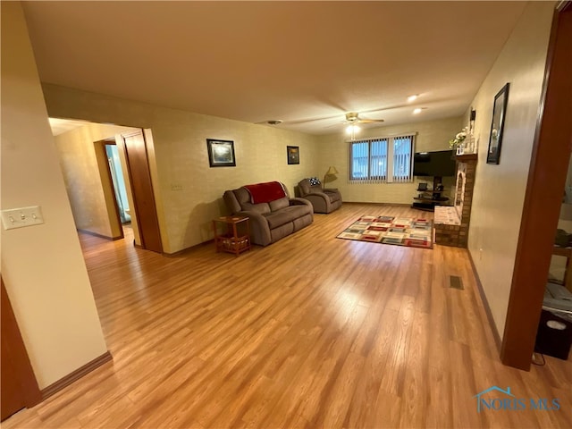 living room with ceiling fan, light wood-type flooring, and a fireplace