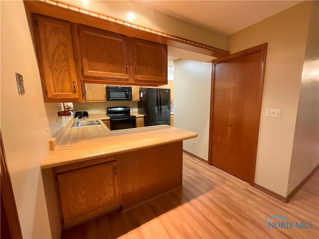 kitchen with kitchen peninsula, black appliances, light hardwood / wood-style floors, and sink