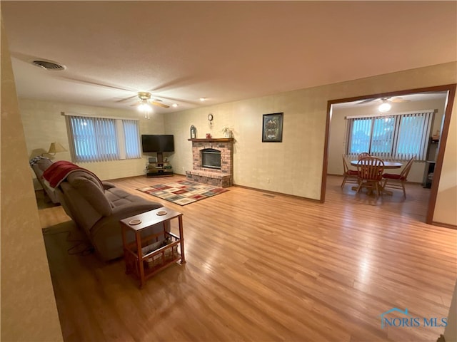 living room with a brick fireplace, light wood-type flooring, and ceiling fan