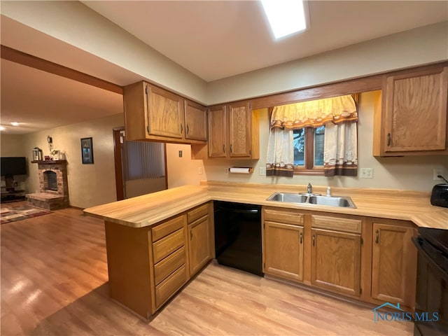 kitchen featuring kitchen peninsula, a fireplace, light wood-type flooring, black appliances, and sink