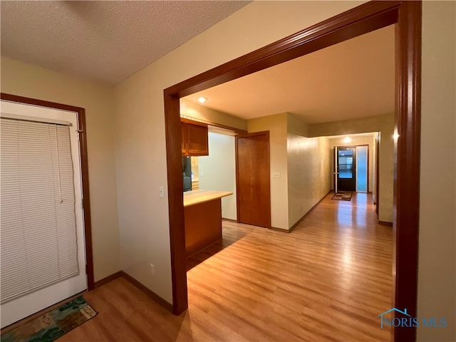 hallway with a textured ceiling and light hardwood / wood-style floors