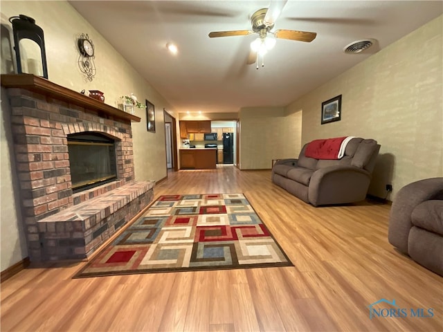 living room featuring a brick fireplace, light hardwood / wood-style floors, and ceiling fan