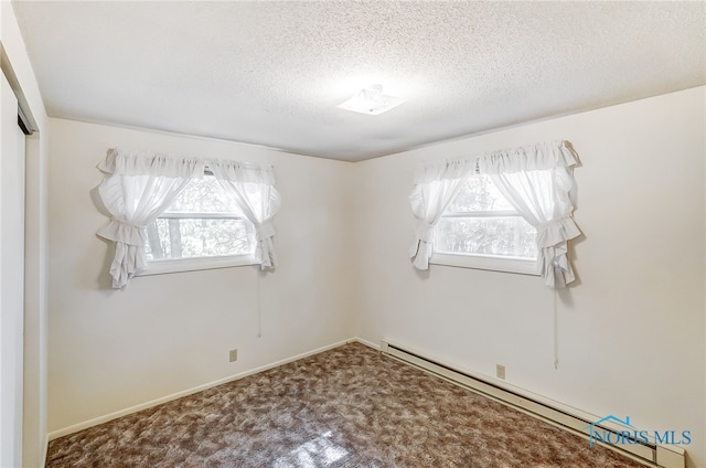 carpeted spare room with a baseboard heating unit and a textured ceiling