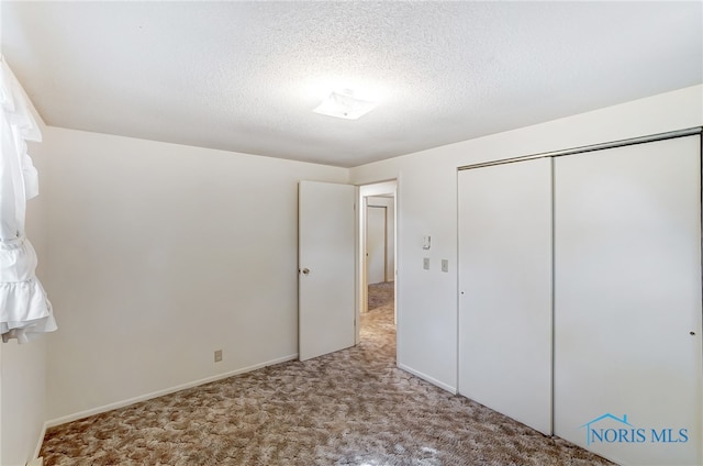 unfurnished bedroom featuring light colored carpet, a textured ceiling, and a closet