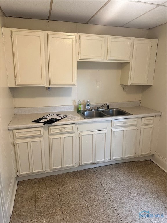 kitchen with a drop ceiling, white cabinetry, and sink