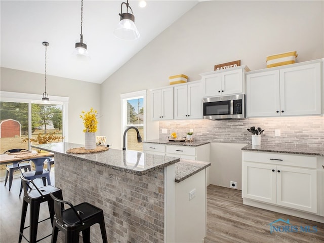 kitchen with a kitchen island with sink, high vaulted ceiling, white cabinetry, light hardwood / wood-style flooring, and decorative light fixtures