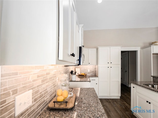 kitchen with dark stone countertops, dark hardwood / wood-style flooring, decorative backsplash, and white cabinets