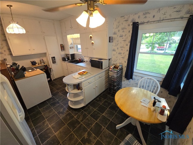 kitchen featuring ceiling fan, white cabinets, hanging light fixtures, kitchen peninsula, and dark tile patterned floors