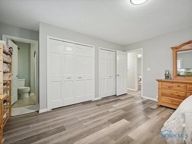 bedroom featuring a textured ceiling, ensuite bath, multiple closets, and hardwood / wood-style flooring