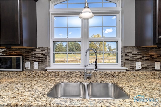 kitchen featuring a healthy amount of sunlight, light stone countertops, sink, and backsplash