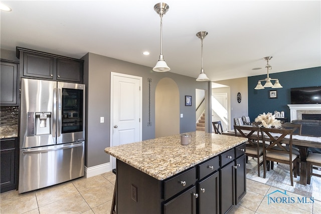 kitchen featuring a center island, decorative light fixtures, light stone counters, stainless steel refrigerator with ice dispenser, and light tile patterned floors