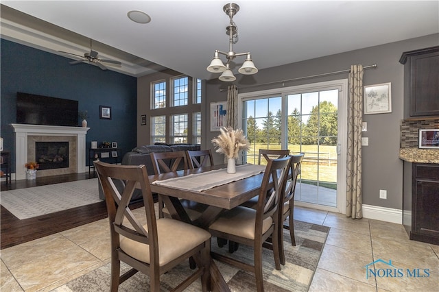 dining area with ceiling fan with notable chandelier, a fireplace, and light wood-type flooring