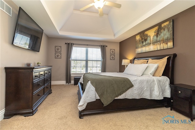 carpeted bedroom with ceiling fan and a raised ceiling