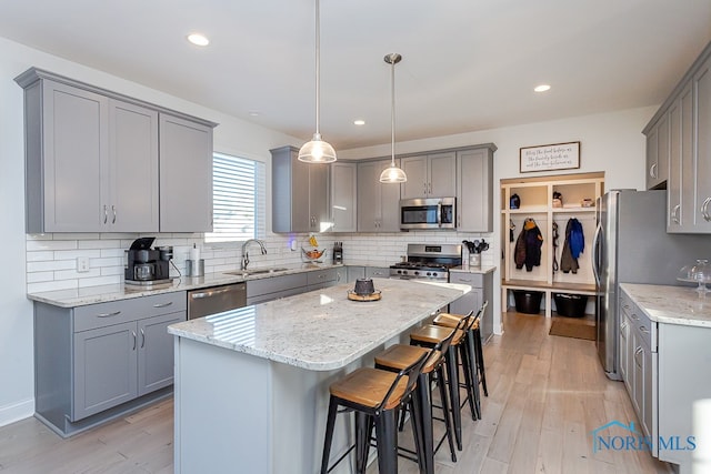 kitchen featuring gray cabinetry, stainless steel appliances, decorative light fixtures, sink, and a center island