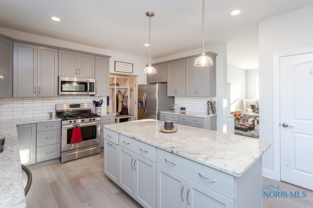 kitchen featuring gray cabinetry, a kitchen island, appliances with stainless steel finishes, hanging light fixtures, and light hardwood / wood-style flooring