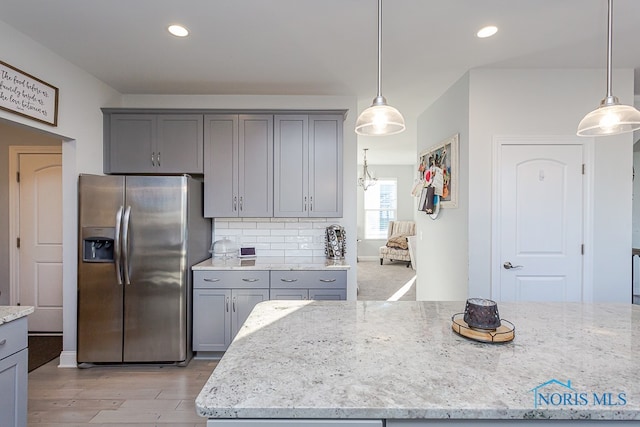 kitchen featuring stainless steel refrigerator with ice dispenser, gray cabinetry, light stone countertops, light hardwood / wood-style flooring, and decorative light fixtures