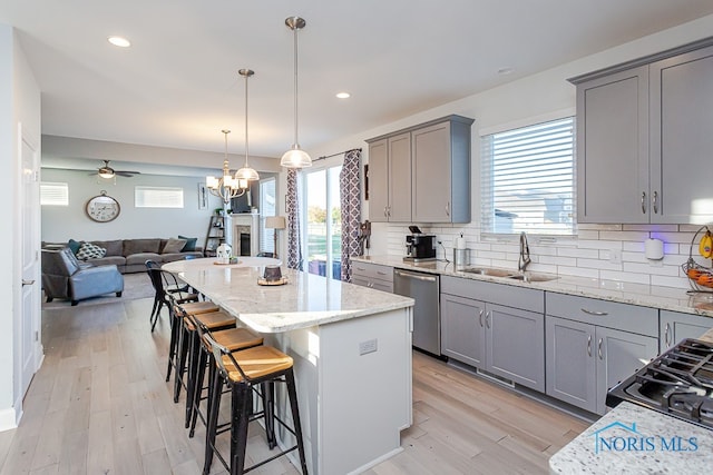 kitchen featuring sink, a kitchen breakfast bar, stainless steel dishwasher, a kitchen island, and light hardwood / wood-style flooring