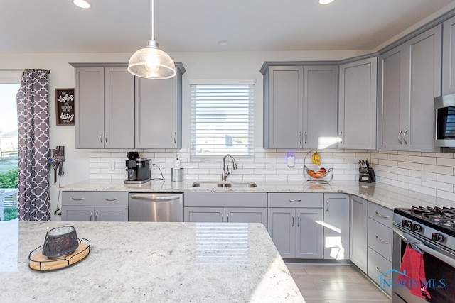 kitchen featuring sink, light stone counters, appliances with stainless steel finishes, decorative light fixtures, and light wood-type flooring