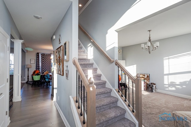 stairs with decorative columns, a chandelier, and wood-type flooring