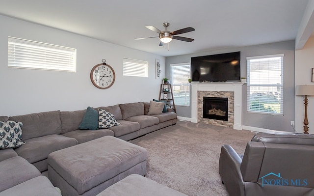 carpeted living room with ceiling fan and a stone fireplace