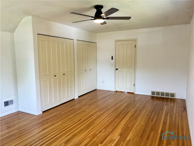 unfurnished bedroom with wood-type flooring, ceiling fan, and multiple closets