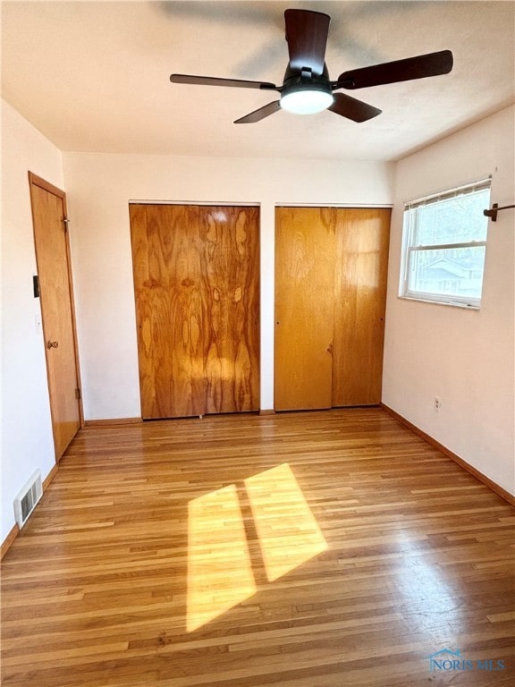 unfurnished bedroom with two closets, light hardwood / wood-style floors, and ceiling fan