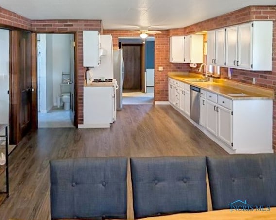 kitchen with white cabinetry, sink, dark wood-type flooring, brick wall, and stainless steel dishwasher