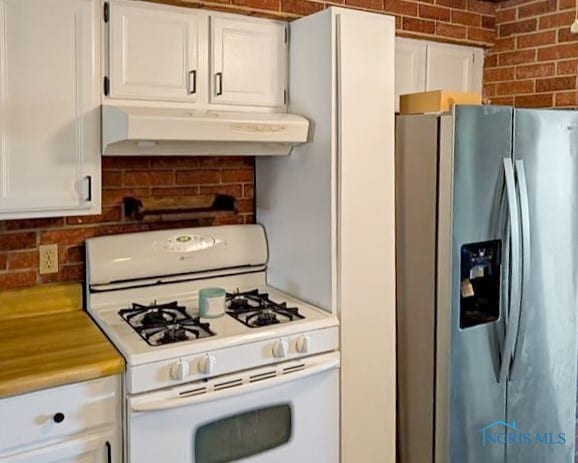 kitchen featuring white cabinetry, white range with gas cooktop, stainless steel fridge, and brick wall