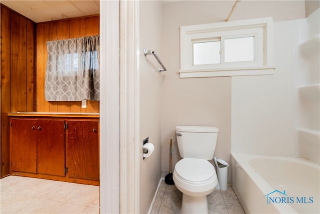 bathroom with tile patterned floors, a bathtub, toilet, and wooden walls